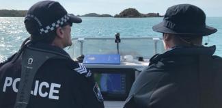 Two people, one in police uniform, driving a boat