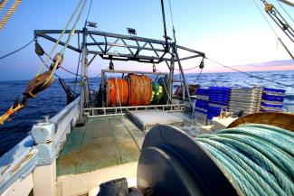 view looking out over the back deck of a commercial fishing boat with fishing nets coiled up and boxes neatly stacked.